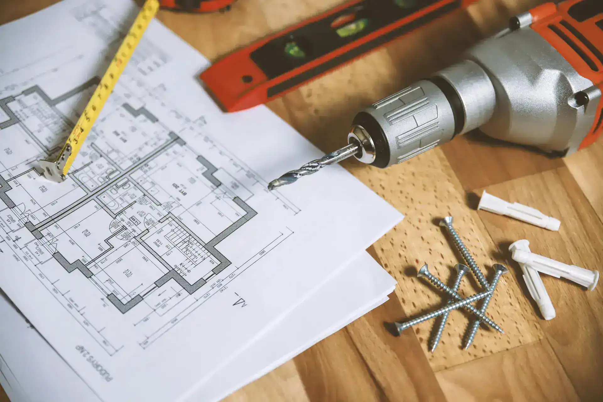 Bespoke worktop planning with drill, screws and measuring tape laid over kitchen design drawings